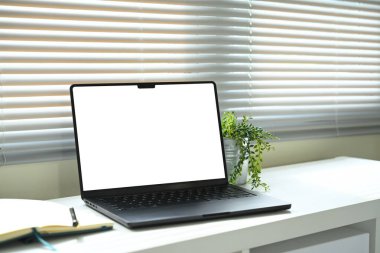 Çalışma alanı dizüstü bilgisayar, defter ve saksı bitkisi beyaz masanın üzerinde doğal ışık altında..