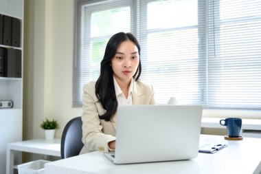 Modern ofiste online bir toplantı sırasında dizüstü bilgisayarda çalışan odaklanmış iş kadını.