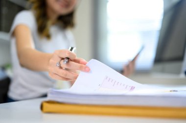 Ofisteki bir kalemle iş belgelerini karıştıran kadına yakın dur..