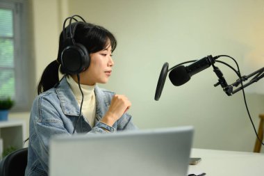 Dişi podcaster ses içeriğini evde dizüstü bilgisayar ve ses donanımı ile kaydediyor.