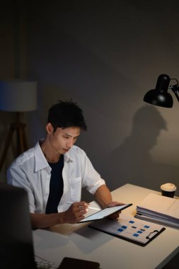 İşadamı belgeleri analiz ediyor ve ofis masasındaki dijital tablete not alıyor..