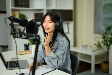 Kadın içerik oluşturucu masadaki dizüstü bilgisayarla mikrofona konuşurken ses kaydediyor.