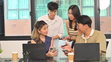 Modern bir ofiste dizüstü bilgisayarın etrafında beyin fırtınası yapan yaratıcı bir ekip..