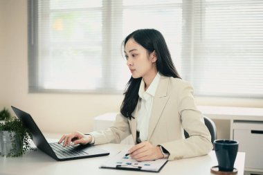 Ofis işleri ve veri analizi için dizüstü bilgisayar kullanan bej ceketli odaklanmış iş kadını.