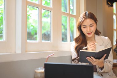 Kendine güvenen bir iş kadını dizüstü bilgisayarının yanındaki bir günlüğe not alıyor..