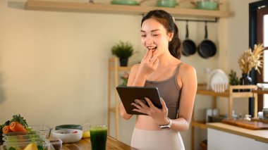 Mutfakta tarifli tablet kullanan genç bir kadın..
