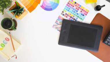 Renk palet çizelgeleri, çizim tableti ve kahve fincanı olan grafik tasarımcı masasının üst görünümü.