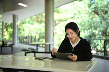 Okulun kampüsünde dijital tablet ve stil eğitimi alan odaklanmış lise öğrencisi..