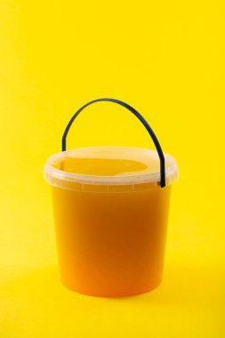 Sarı zemin üzerinde bal olan şeffaf bir kova.