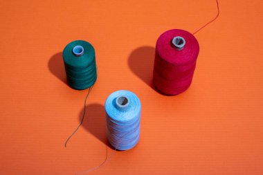 Renkli arkaplanda renkli iplikleri olan üç bobin.