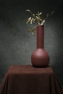 Still life with a brown vase and branches of a plant on a brown table
