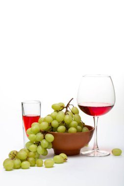 Tabakta olgun üzümler, beyaz arka planda bir bardakta içki.