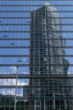 Pencerelerinde yansımalar olan çok katlı modern bir binanın ön cephesi.