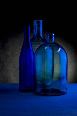 Karanlık bir arka planda üç cam şişe ile sakin bir hayat
