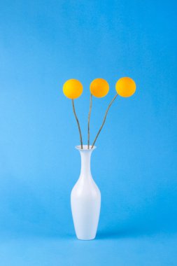 Mavi bir arka plan üzerinde bir vazo ve turuncu topları ile soyut natürmort