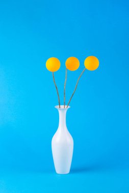 Mavi bir arka plan üzerinde bir vazo ve turuncu topları ile soyut natürmort