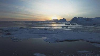 Antarktika sahilinde şafak vakti. Kutup gecesi gün batımı. Okyanus buzla kaplı. Havadan bakıldığında üstte. Antarktika kar dağı. Gökyüzü gündoğumu Antarktika kışı. Açık deniz. Güzel gökyüzü manzarası. Üst İHA Uçuşu