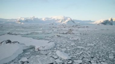 Antarktika sahilinde gün doğumu. Hava görüntüsü. Okyanus eriyen buzla kaplı. Kar dağının üzerindeki Antarktika. Açık deniz kışı. Güzel gökyüzü manzarası. Üst İHA Uçuşu