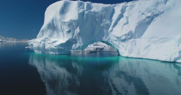 ターコイズ ウォーターの 南極の氷山アーチ 氷河が極海で溶ける バックグラウンドで雪に覆われた山 気候変動 地球温暖化 晴れた日のパノラマ低角度ドローン飛行 — ストック動画
