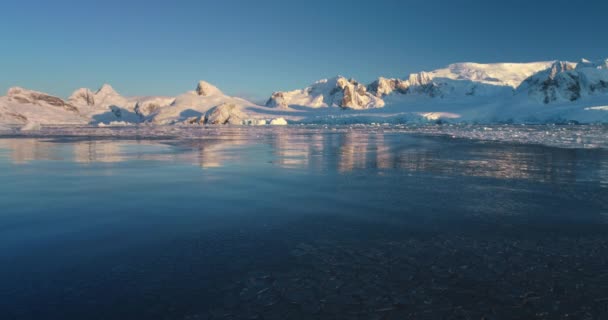 探索南极洲冬季风景中冰冷的奇观 白雪覆盖着山脉 夕阳西下 冰冷冰封的海水 大自然原生态的美丽 北极的场景慢动作低角无人机飞行 — 图库视频影像