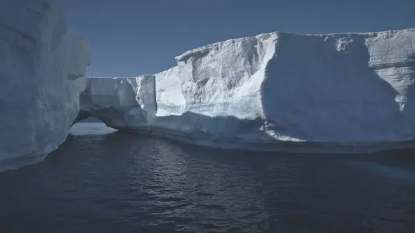 Iceberg Arch Antarctic Ocean Glacier Seascape. Hole in Massive Ice Berg Floating in Arctic Blue Water Sea at Greenland. Global Warming Concept Landscape Shot Footage 4K UHD
