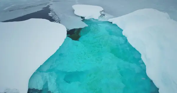 Melting arctic blue water glaciers aerial view. Snow covered iceberg with melted turquoise hole inside. Polar climate change. Arctic winter landscape, global warming problem. Close up drone flight