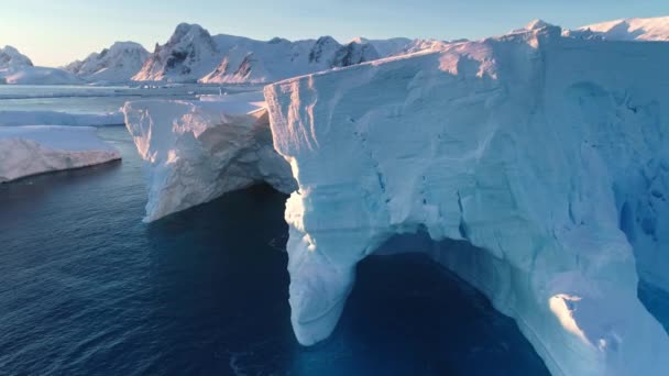 巨大的冰山 蓝色的洞穴 融化的冰川在南极洲 大量浮冰漂浮在极地海水中 在粉红色的夕阳下 雪覆在群山之上 南极旅行 北极风景 无人机飞行 — 图库视频影像