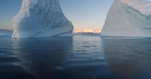 2つの巨大な青い氷山が極地で溶けている 低い角度は タワーリング氷河の穴間の穏やかな海面上のドローン飛行を閉じます エコロジー 溶ける氷 気候変動 地球温暖化の概念 — ストック動画