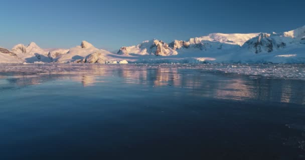 白雪覆盖的高山高耸在海洋湾 色彩斑斓的落日在冰冷平静的冰水波中反射 南极旅行和探险 北极冬季自然背景景观 静态射击 — 图库视频影像