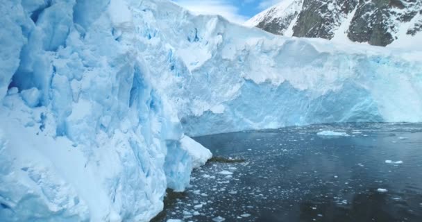 覆盖着大雪的冰川在冰冷 黑暗的海水之上升起 冰墙形成 冰山在明亮的天空下漂浮 山体背景为斜坡 南极极地景观近景全景 — 图库视频影像