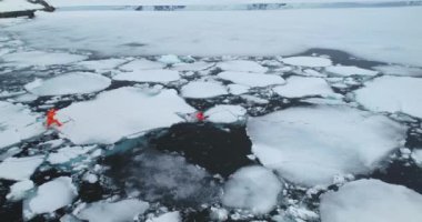 Dalış kıyafetleri içindeki iki adam eriyen kutup buzunu çalıştırıyor. Turuncu dalgıç elbiseli insanlar kutup tuzağından kaçmaya çalışır, soğuk suyun altına düşerler. Küresel iklim ısınmasının buzulları erittiğini araştırın. Hava görüntüleri