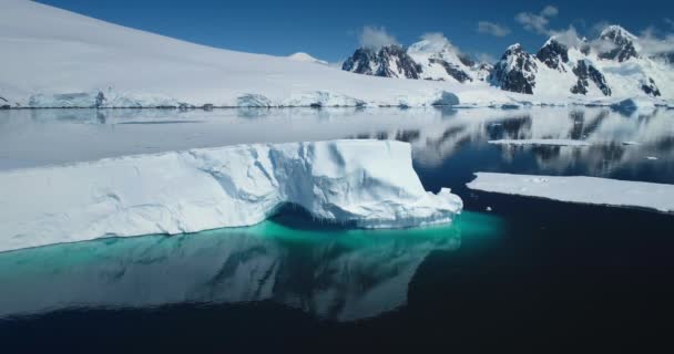 南极巨大的高耸的冰山在阳光灿烂的日子里漂浮在极地的海洋上 覆盖着积雪的山脉和背景中的冰川反映在水晶水中 北极冬季景观与全球变暖问题 — 图库视频影像