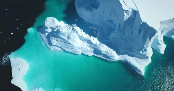 Melting snow covered glacier in blue water aerial top view. Nature beauty towering floating iceberg. Polar winter landscape. Ecology, melting ice, climate change, global warming background. Drone shot