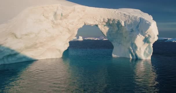 融化的冰洞拱形冰山高耸着北冰洋 大冰川在日落时漂浮着冷水 生态学 融化的冰 气候变化和全球变暖的概念 无人机飞行接近变焦 — 图库视频影像