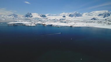 Antarktika mavi okyanus suyu Aerial manzara. Antarktika Okyanusu Açık Su Yüzeyi. Arka planda vahşi doğa karlı dağ sıraları var. Güney Kutbu Dağ Manzarası İnsansız Hava Aracı Uçuş Görüntüsü