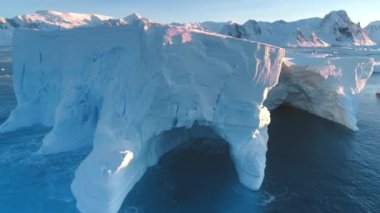 Antarktika 'da gün batımında yükselen dev buzdağı. Okyanus dalgalarıyla yıkanan eriyen buzullar ve mağaralar. Güneşli kış gününde kutup iklimi değişikliği. Kuzey Kutbu kış manzarası. Küresel ısınma sorunu.