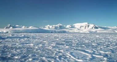 Antarktika 'daki karlı dağ manzarasının üzerinden uç. Kutup donmuş okyanus manzarası mavi güneşli gökyüzünün altında karla kaplıdır. Güney Kutbu 'nun güzelliğini keşfedin. Antarktika seyahat ve keşif arkaplanı