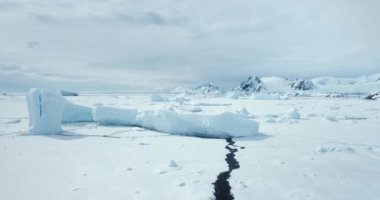 Donmuş okyanusta düşen buzulun devasa buzdağı. Kar ve buzdan oluşan çöl beyazları diyarı. Arka planda sıradağlar var. Antarktika seyahati ve keşfi. Güney Kutbu 'nun güzelliğini keşfedin