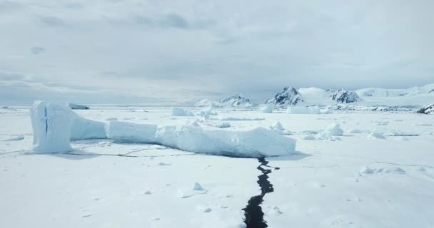 氷河が崩壊した氷河の氷山が凍った海に浮かぶ 砂漠の白い雪と氷の国 バックグラウンドの山脈 南極大陸を旅して探検 南極の美しさを発見する — ストック動画