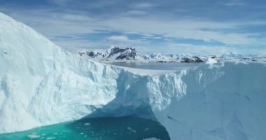 Antarktika 'daki eriyen buzulun üzerinde insansız hava aracı uçuşu. Mavi gökyüzünün altında yükselen dağların yanında devasa bir buz dağı sürükleniyor. Kuzey Kutbu kış manzarası küresel ısınma. İklim değişikliği