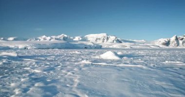 Antarktika karla kaplı, arka planda yüksek sıradağlarla kaplı kış manzarası. Donmuş kutup okyanusu kıyısında İHA uçuşu. Antarktika gezisi keşfi. Güney Kutbu 'nun güzelliğini keşfedin