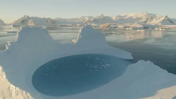 Close-up iceberg pool. Antarctica aerial view drone flight . Slow motion zoom the white iceberg with oval blue clear water pool next to the Antarctic continent. Snow covered mountains background.
