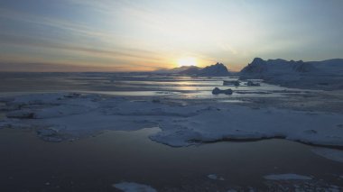 Antarktika sahilinde şafak vakti. Kutup gecesi gün batımı. Okyanus buzla kaplı. Havadan bakıldığında üstte. Antarktika kar dağı. Gökyüzü gündoğumu Antarktika kışı. Açık deniz. Güzel gökyüzü manzarası. Üst İHA Uçuşu