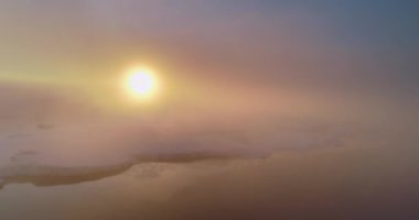 Antarktika 'da gündoğumu sisi üzerinde uçan bir hava. Sabah güneşi karla kaplı tepe okyanusundaki bulutların arasından parlıyor. Destansı manzara, parlak turuncu güneş yükseliyor. Doğa yolculuğu arka planı