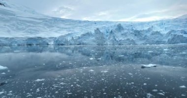 Antarktika sularında devasa mavi buzullar yükseliyor. Karla kaplı buzdağı yansıması buz gibi okyanusu yüzdürür. Ekoloji, eriyen buz, iklim değişikliği ve küresel ısınma kavramı. Düşük açılı İHA uçuşu