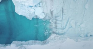 Okyanus dalgalarıyla yıkanan mavi su havuzlu donmuş buz mağarası. Eriyen buzul yukarıdan aşağıya bakıyor. Buzul desenli arka plan. Kuzey Kutbu kış manzarası küresel ısınma. Antarktika 'da iklim değişikliği