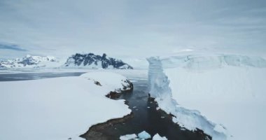 Antarktika kış manzarası hava manzarası. Kayalık okyanus koyunun üzerinde yükselen buzullar, arka planda karla kaplı dağlar. Kutup doğasında büyük bir buz duvarı var. Güzel Güney Kutbu seyahat görüntüleri