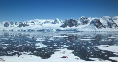 Amazing Antarctica winter landscape. Snow covered mountains towering polar ocean under bright blue sky. Ice floes icebergs melting in sunny day. Ecology, climate change, global warming. Aerial shot