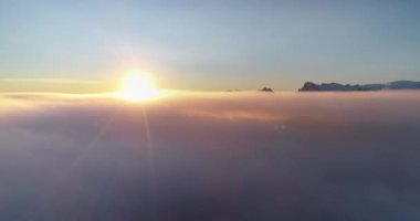 Güneş mavi gökyüzünün altında sabah bulutları üzerinde ışıldıyor. Hava manzaralı parlak renkli gündoğumu sisi. Arka planda kış sıradağları. İHA uçağı kalkıyor. Doğa arka planı mükemmel manzara duvar kâğıdı
