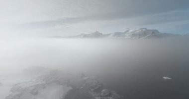 İnsansız hava aracı Antarktika okyanusu üzerinde sisli gökyüzü, karlı dağ zirveleri, arka planda gündoğumu bulutları. Antarktika sahilinde sabah sisi, sis bulutu. Hava manzaralı yüzey. Vahşi doğa arka planı